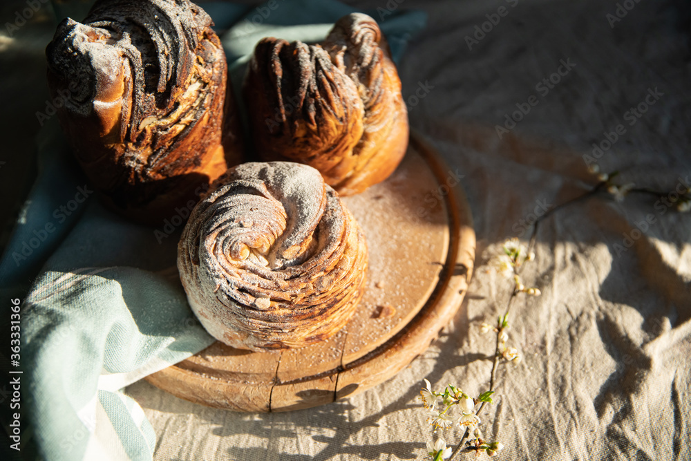 Homemade cruffin breads with dried fruits, cocoa and cinnamon fillings on wooden board and blooming cherry twig on linen tablecloth . Homemade cruffin breads with dried fruits, cocoa and cinnamon fillings on wooden board and blooming cherry twig on linen tablecloth .
