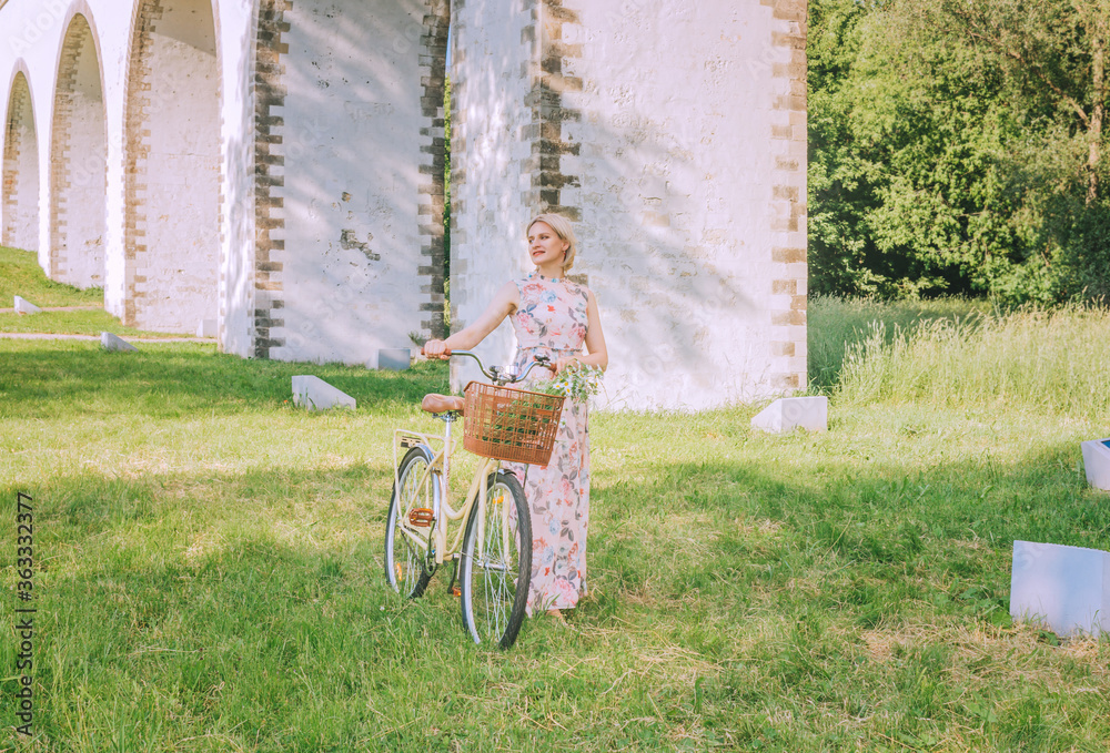Fototapeta premium Pretty woman with her bicycle on the bridge aqueduct background in summertime season