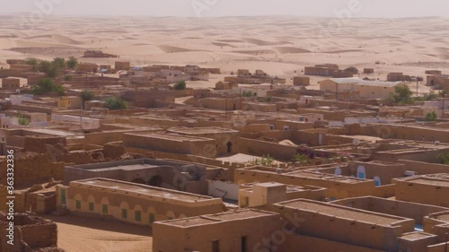 Aerial drone tracking shot flying over the rooftops of the desert town Chinguetti in Mauritania with the desert and sand dunes in the background going off into the distance. 