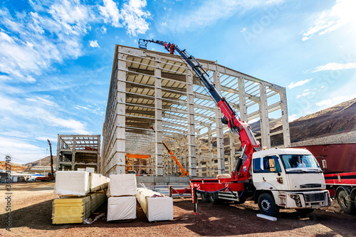The crane (HIAB) extend its lift bucket to roof of the new building for isolation in the construction site. It is a Swedish manufacturer of loader cranes, demountable container handlers.