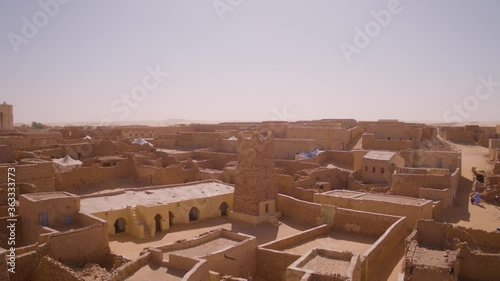 Aerial drone shot rising from rooftop level into the air to reveal the desert town of Chinguetti in Mauritania surrounded by the sahara desert in the background landscape.