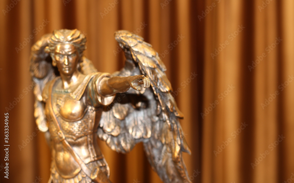 A bronze statuette of the Archangel Michael points a finger forward.