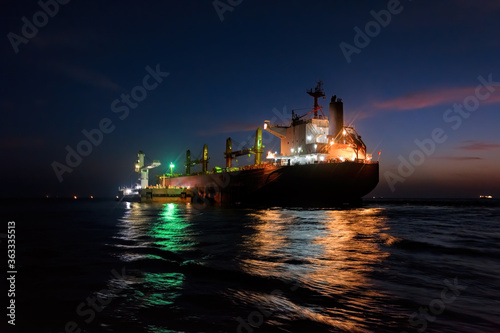 Night loading big mother sea bulk carrier ship with Bauxite aluminium ore from the mini bulk carrier (feeder) vessel at offshore Kamsar port, Guinea, West Africa.