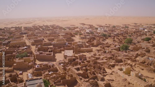 Aerial drone orbit shot of the desert town Chinguetti in Mauritania. Circling the town centre from above showing the entire town surrounded by Sahara desert dunes in the distance.
