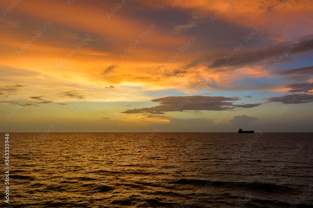 Incredible sunset over sea with a silhouette of a cargo vessel.