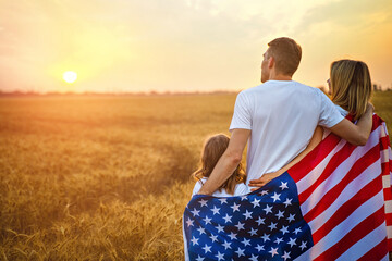 Back view of a unrecognizable Happy family in wheat field with USA, american flag on back.