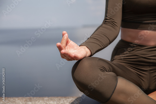 Beautiful brunette in a green suit does yoga by the water. Yoga in the open. Individual yoga class.