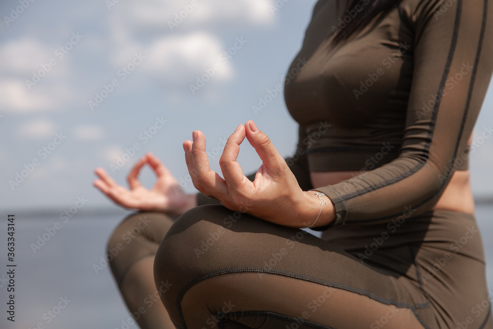 Beautiful brunette in a green suit does yoga by the water. Yoga in the open. Individual yoga class.