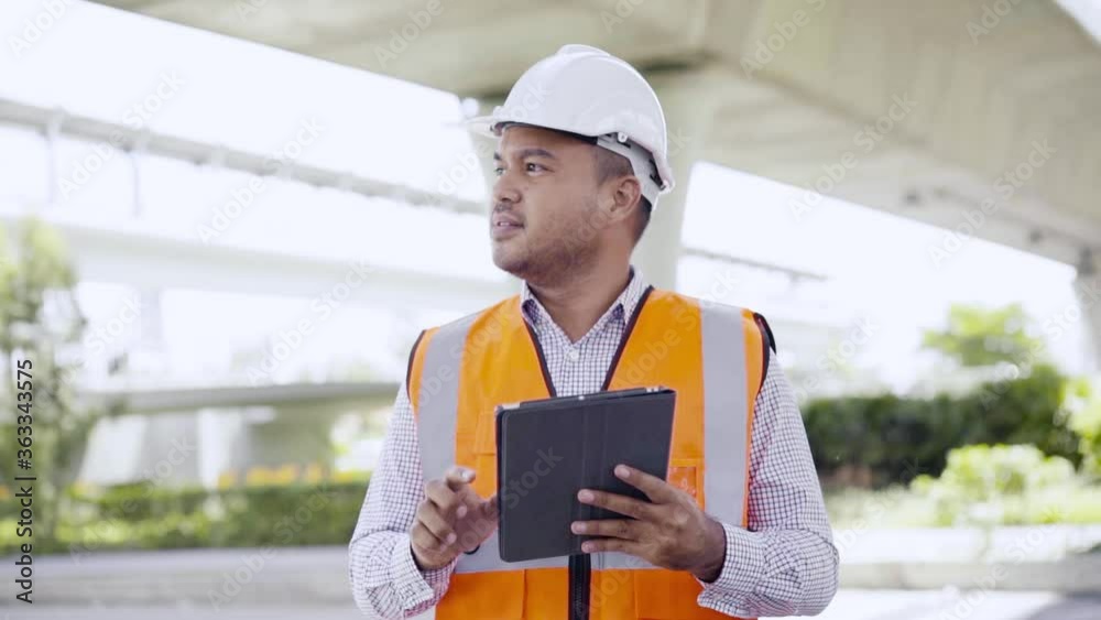 Asian civil engineer operate with tablet to control working at construction. Worker wearing hard hat at highway concrete road site. Asian civil engineer operate with tablet to control working at construction. Worker wearing hard hat at highway concrete road site.