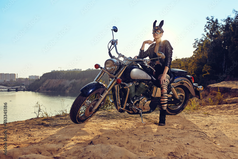 Obraz premium A beautiful sexy young woman in leather jackets and rabbit mask sitting on a black and chrome motorbike