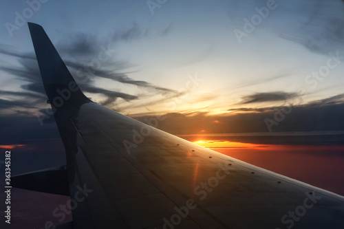 Wing of a flying airplane on a background of sun rays at sunset