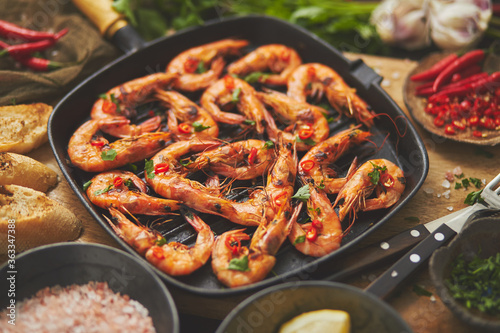 Tasty appetizing roasted shrimps prawns with spices on pan with ingredients on rusty background