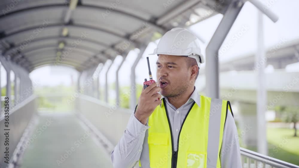 Asian civil engineer operate with radio to control working at construction. Worker wearing hard hat at highway concrete road site. Traffic report concept. Slow motion shot. Asian civil engineer operate with radio to control working at construction. Worker wearing hard hat at highway concrete road site. Traffic report concept. Slow motion shot.