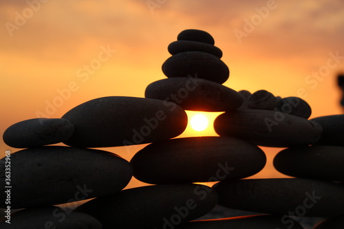 Pyramid of stones on the beach with sunset sun background