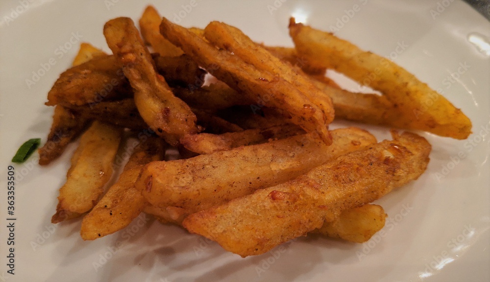 A closeup view of spicy and crispy chili potato served beautifully in a white plate A closeup view of spicy and crispy chili potato served beautifully in a white plate