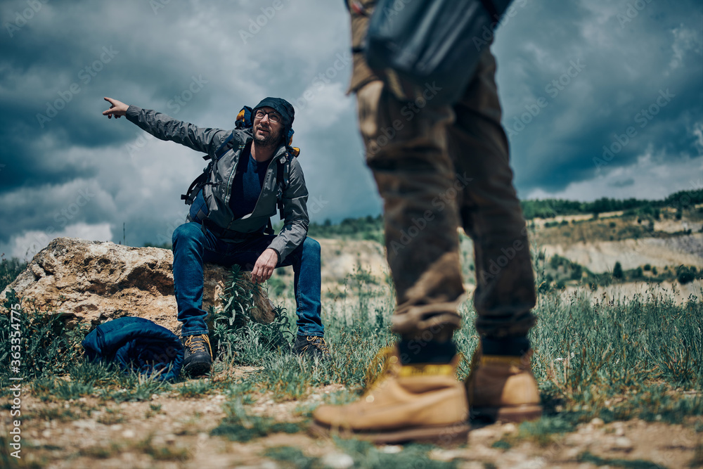 Two man at camping trip. One man sitting on rock and pointing at right way while other one standing. Two man at camping trip. One man sitting on rock and pointing at right way while other one standing.