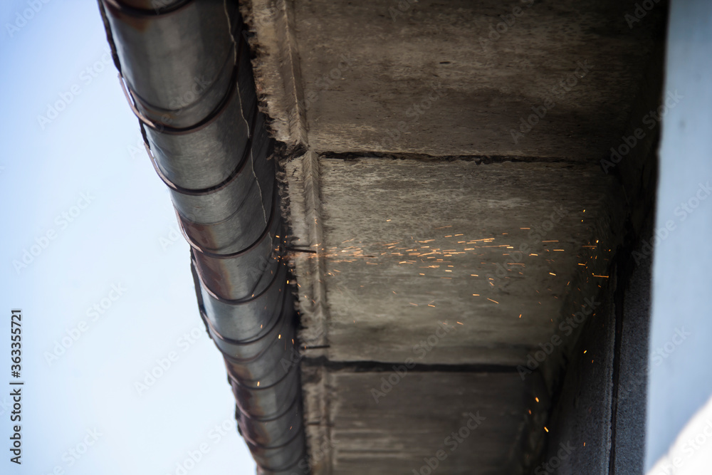 Obraz premium Replacement gutter system with Welding machine for a metal roof. Holder gutter drainage system on the roof. Cut off a gutter system on the roof.