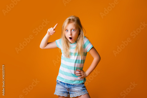 portrait of a happy blonde girl in a blue T-shirt on a yellow background. child's emotions, space for text