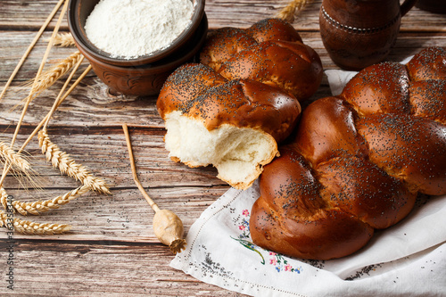 Homemade Jewish traditional challah bread on white napkin on wooden table. Homemade Decorated with poppy seeds. Jewish cuisine. Copy space for text, brand or logo. Close up and top view