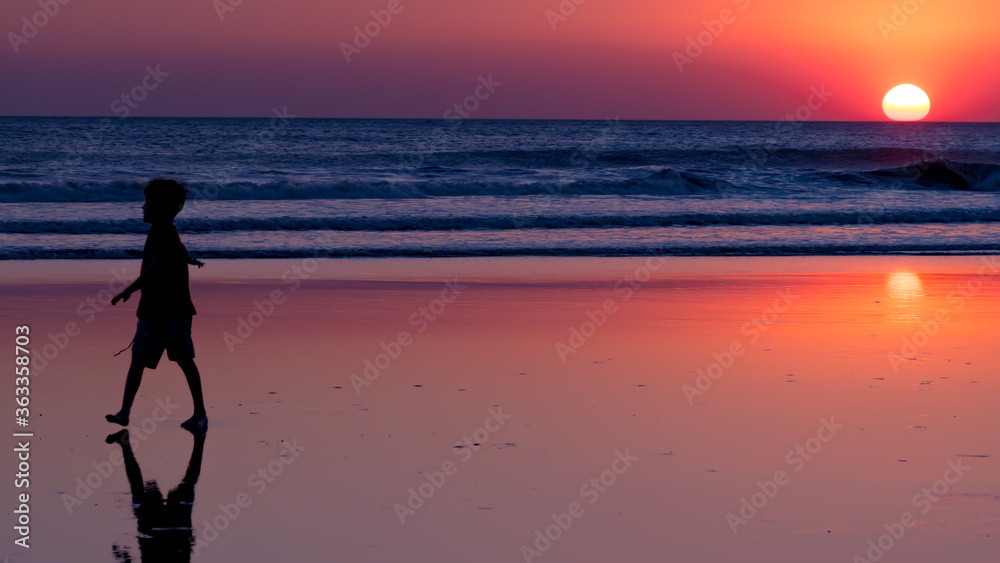 Fototapeta premium a child plays on the beach, backlight and sunset.
