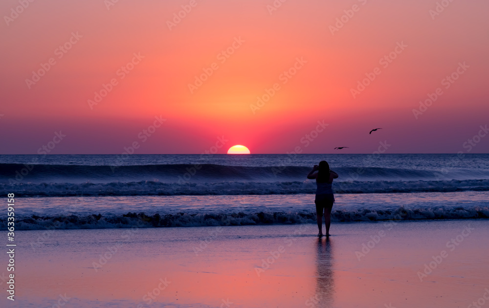 Girl takes a photo of the sunset on the beach, birds, shadows, sunset. 