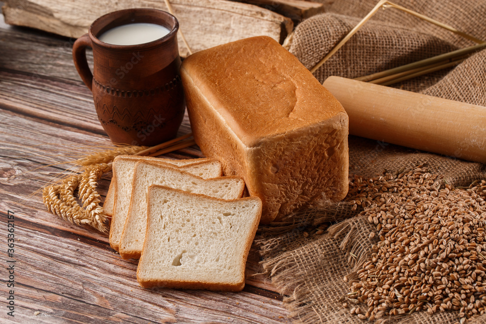 Close-up of homemade bread. Peasant square bread and wheat spikelets with space for text. Homemade baking. White bread with flour and milk on wooden chopping board wheat rye ears copy space.
