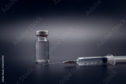 Small vaccine bottle (phial) and a medical syringe injection with a vaccine drop on its needle, isolated on black background