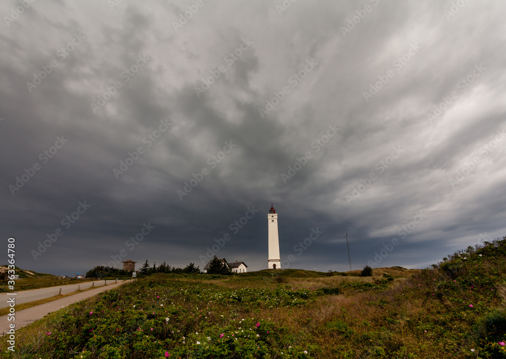 A heavy thunderstorm is catching up over the lighthouse Blåvandshukfyr at the North Sea coast in Denmark causing a dramatic dark grey sky A heavy thunderstorm is catching up over the lighthouse Blåvandshukfyr at the North Sea coast in Denmark causing a dramatic dark grey sky