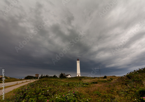 A heavy thunderstorm is catching up over the lighthouse Blåvandshukfyr at the North Sea coast in Denmark causing a dramatic dark grey sky