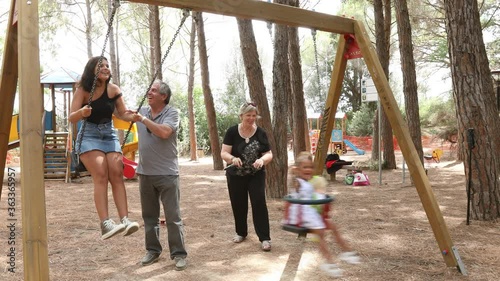 Video in 4k due nonni bianchi giocano divertiti con le lori nipoti brasiliane nell'altalena di un parco giochi. photo