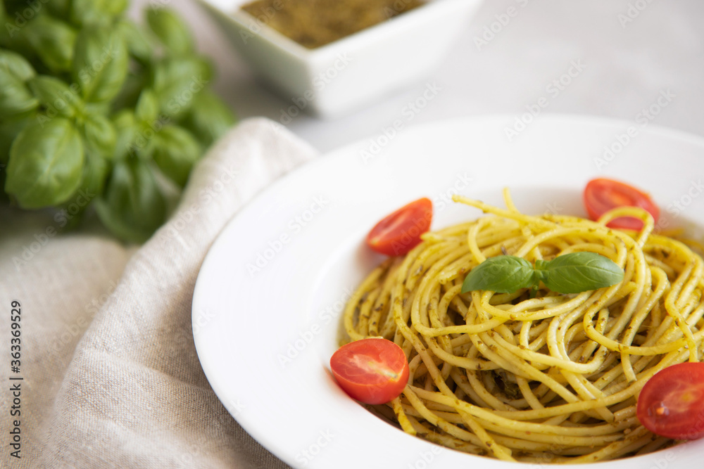 close-up plate with traditional italian pasta pesto with cherry tomatoes, next to a gravy boat with basil sauce.
