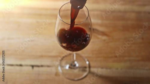slow motion of red wine pouring in wineglass on wooden table photo