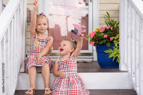 Canvastavla Two cute little girls sitting on the front porch on Fourth of July waving flags