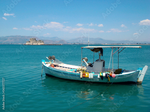 A small fishing boat in a body of water. Venetian castle of Bourtzi in the background, Nafplio city, Argolida, Peloponnese, Greece.