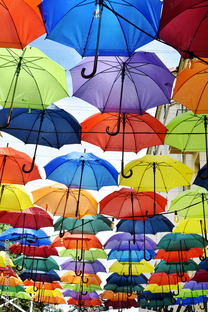 colorful umbrellas hanging between buildings over blue sky