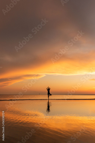 Meditation woman practicing tree yoga pose on the beach at sunset. Copy space. 