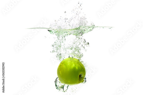 one green apple falling into water on a white background with splashes, drops and bubbles.