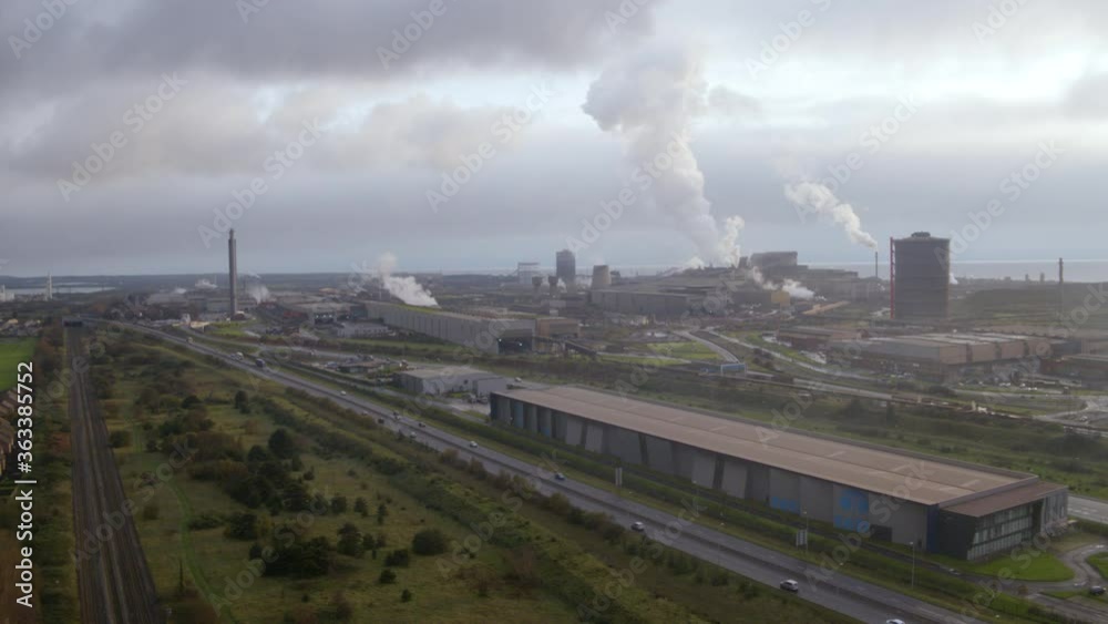 Aerial drone shot of Tata steelworks in Port Talbot, Wales with smoke rising from the chimneys on a cloudy day with main road and traffic in the foreground Aerial drone shot of Tata steelworks in Port Talbot, Wales with smoke rising from the chimneys on a cloudy day with main road and traffic in the foreground