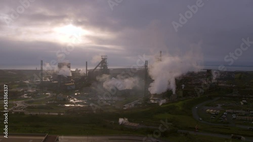 Aerial drone shot of Tata steelworks in Port Talbot, Wales with smoke rising from the chimneys and the sun coming through the clouds in the distance. photo