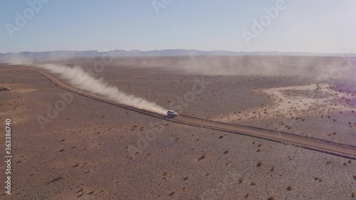 Aerial drone shot of rally car racing along a dirt track road with trails of dust and smoke in the middle of the desert during the Africa eco race or Dakar Rally