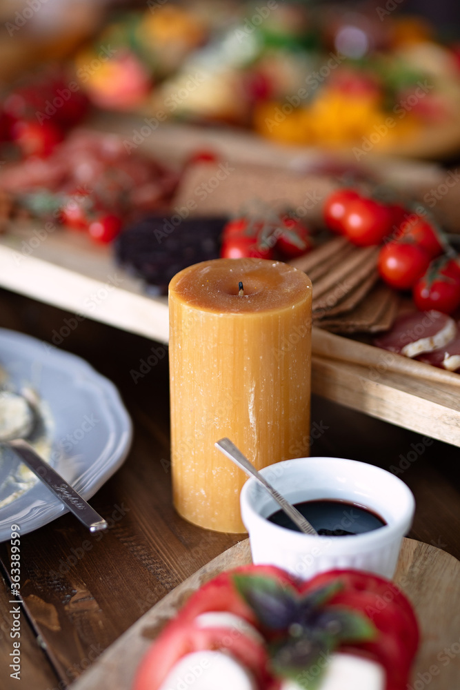 Fototapeta premium brown wax candle stands on table with food, colorful dishes on background, selective focus, festive dinner,