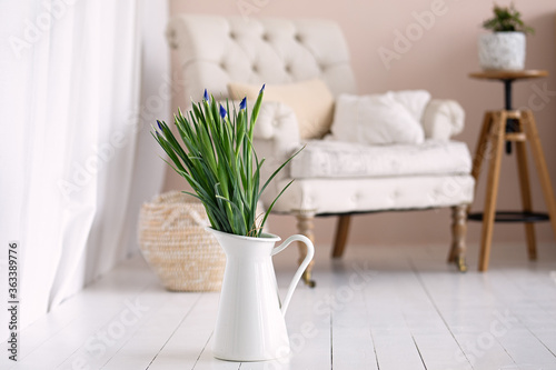 purple flowers with green leaves stand in a white vase, bright room with  beige armchair, Stylish interior, cozy room