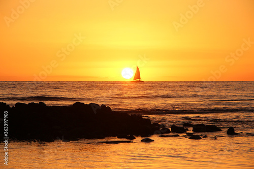 The romantic golden sunset in Hawaii, Big Island. View on the open ocean, sailing boat crossing the sun on the horizon. 