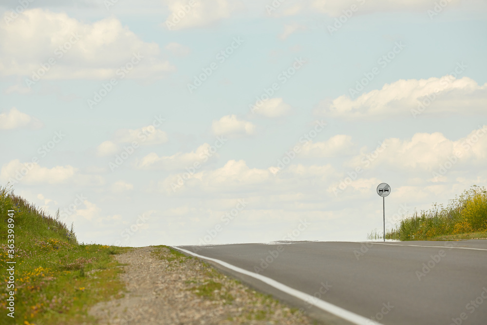 Highway road up hill through green grass field under white clouds on blue sky in summer day. Natural Landscape of Road and Landscape Scenery. Road trip travel concept.