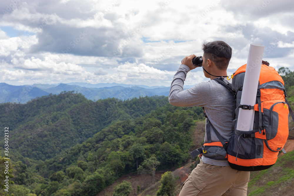 Young man with backpack and holding a binoculars looking on top of mountain