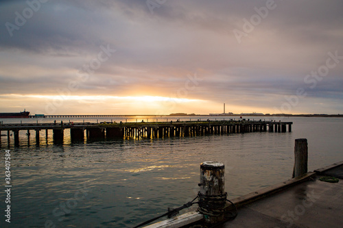 The sun rises through the clouds over the calm sea and wharves in Bluff, New Zealand photo
