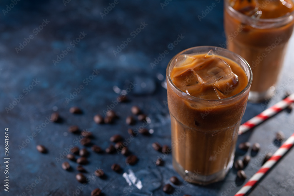 Ice cold coffee with ice cubes and coffee grains on a blue background. Cold summer drink with pipes Ice cold coffee with ice cubes and coffee grains on a blue background. Cold summer drink with pipes