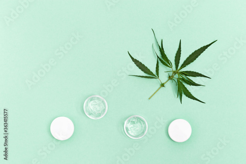Jar with transparent cosmetic product, gel or cream with cannabis oil on green colored background. Flack with of antioxidant cream for eyes. View from above.