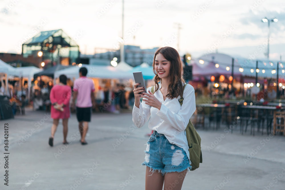 Fototapeta premium Young asian adult woman using smart phone at outdoor night market