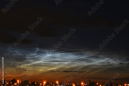 An image of noctilucent clouds over an small urban city during the early morning hours. 